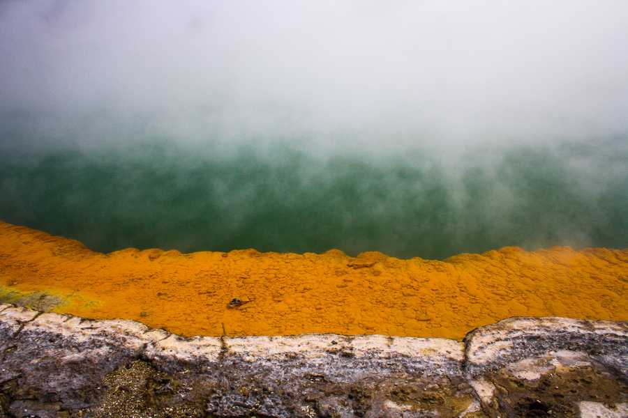 Yellow ochre rock contrasts against the turquoise green water in a geothermal pool.