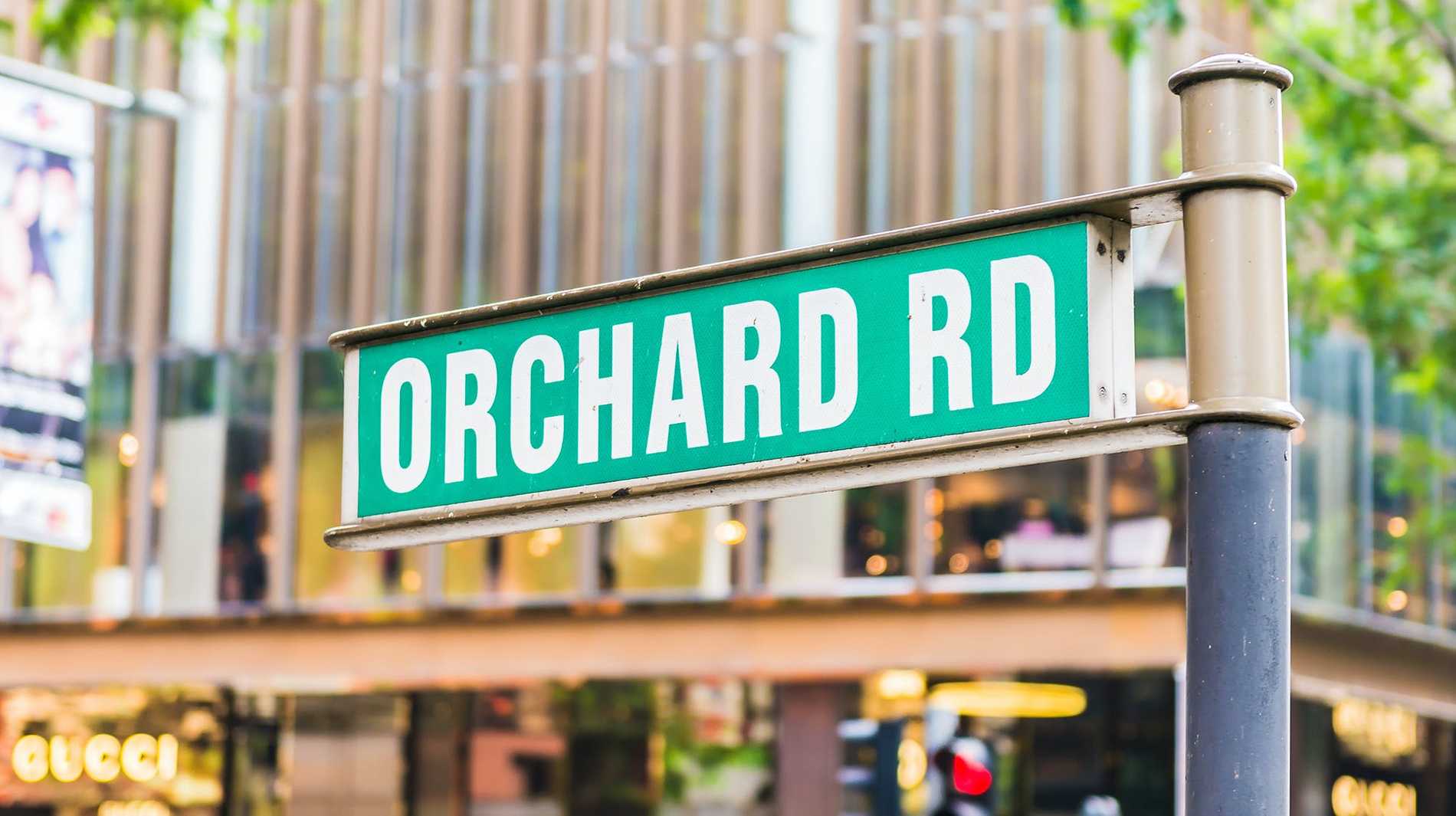 A street sign for Orchard Road in front of one of the many shopping malls along this street.