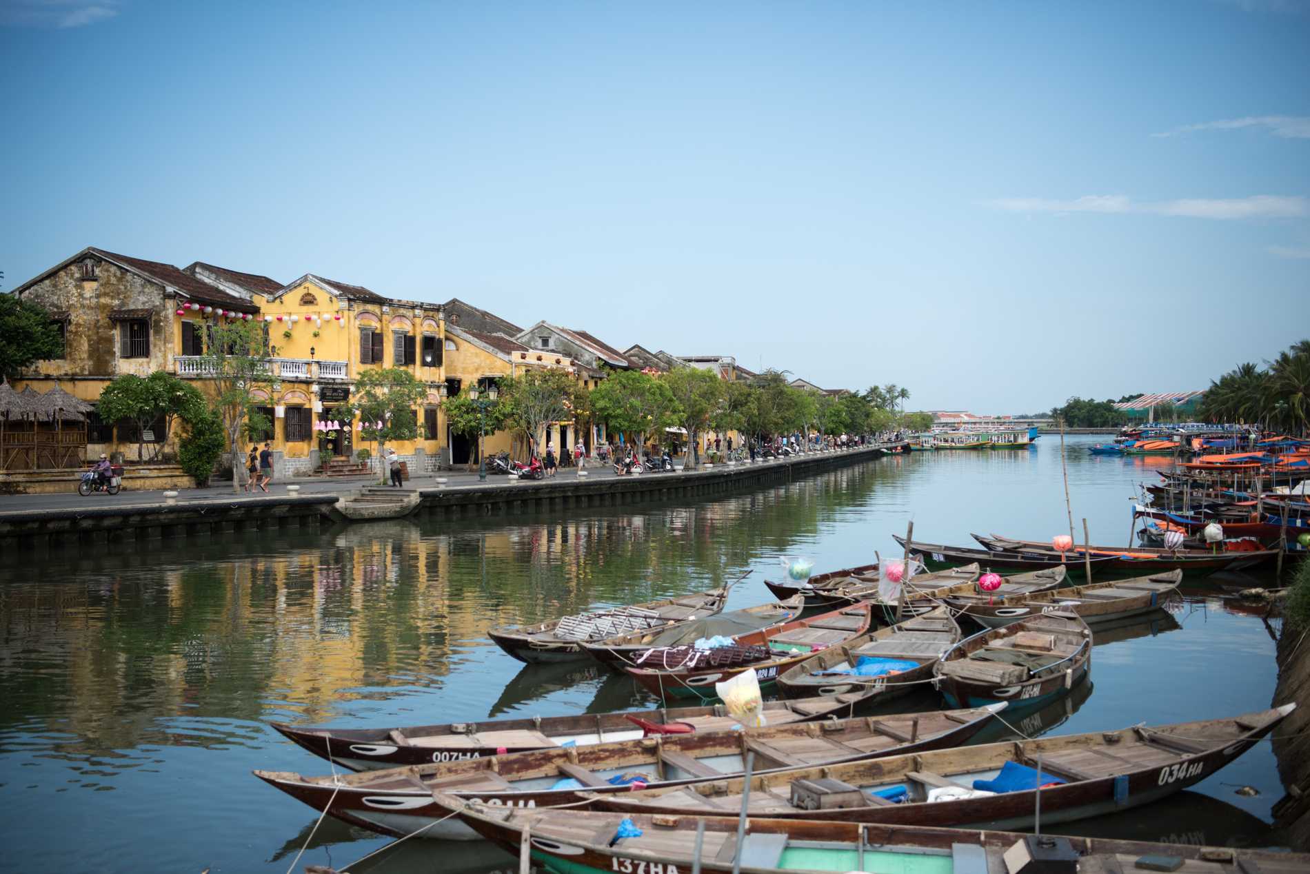 Boats moored up by the side of the river in Hoi An as the traditional yellow buildings reflect in the water.
