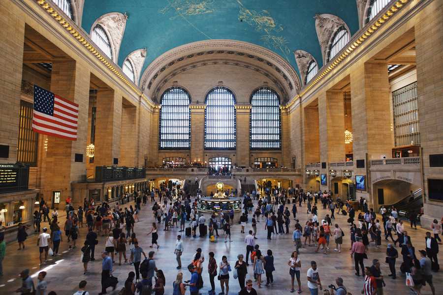 A busy main concourse at Grand Central Station with its vaulted turquoise ceiling covered in golden constellations.
