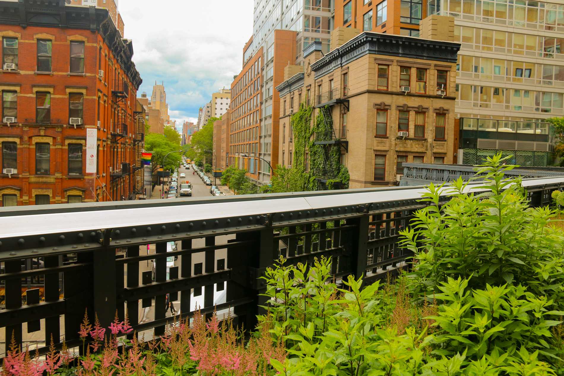 View of a New York City street with red brick buildings taken from the High Line crossing above.