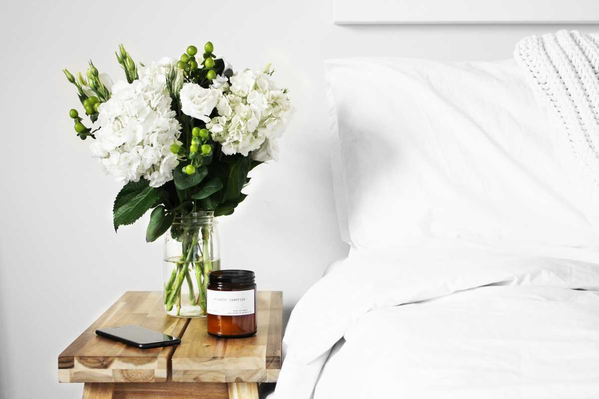A bedside table with a vase of white flowers.
