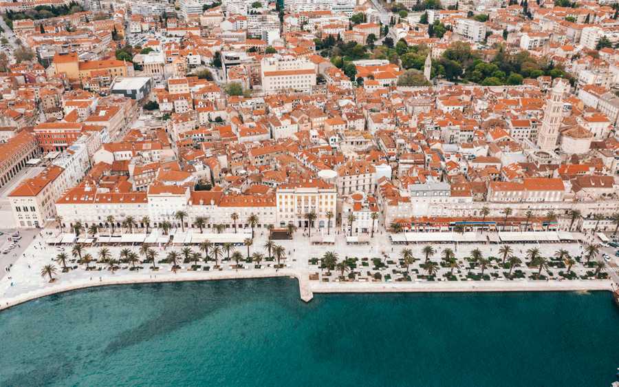 Aerial view of Split's white buildings and red rooftops beside the turquoise Adriatic Sea.